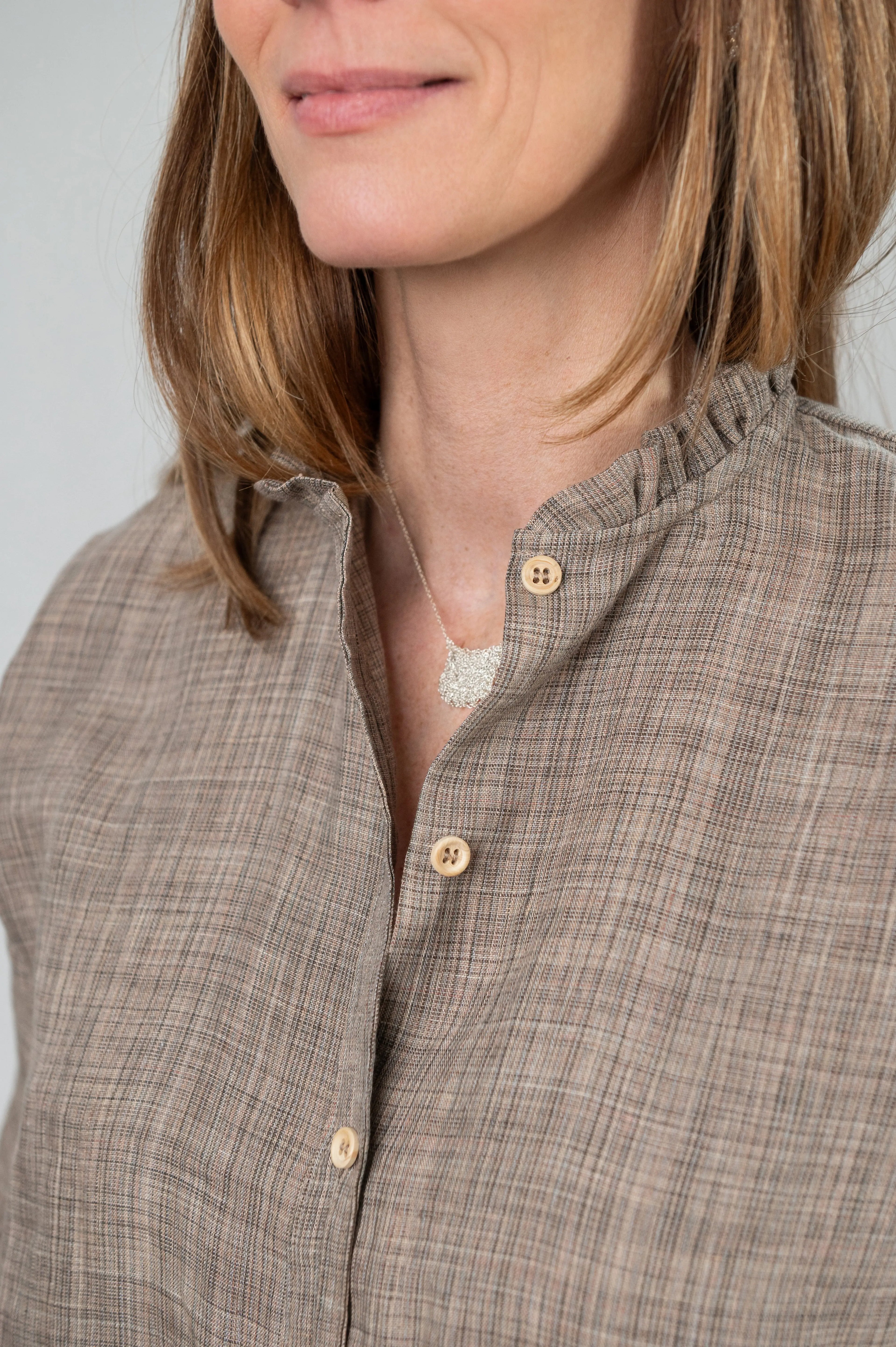 Chemise Narcisse à col froncé en lin couleur grège naturel, détail du col et des boutons en bois, portée avec un collier signé A.no.