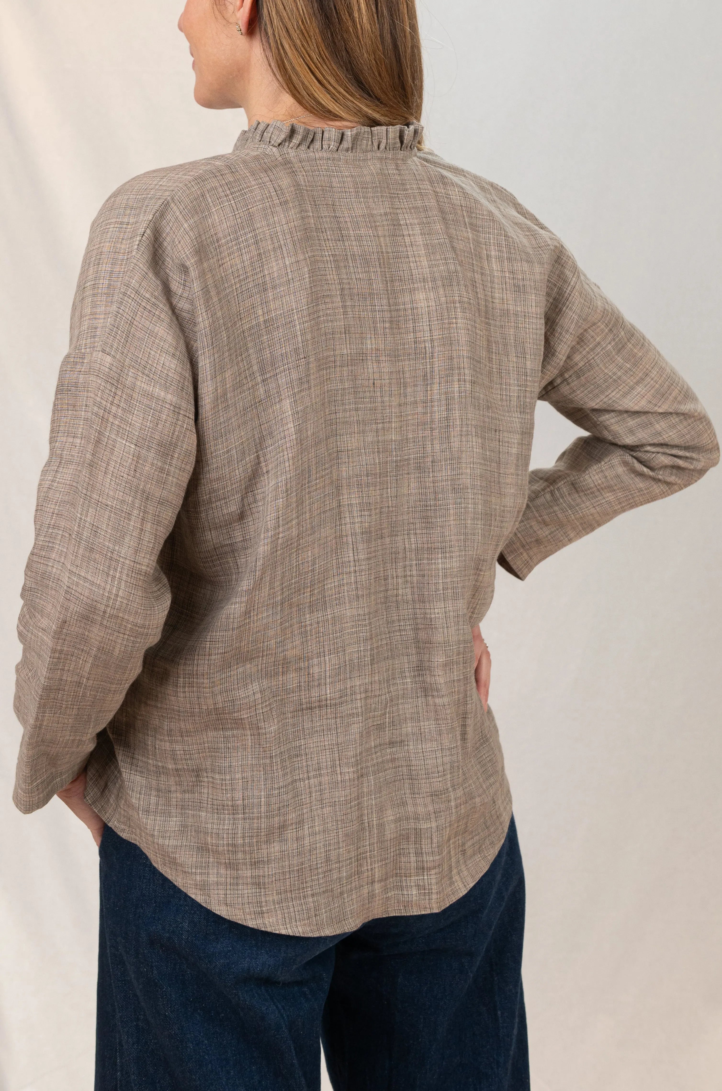 Chemise Narcisse à col froncé en lin couleur grège naturel, vue de dos, portée avec un pantalon Sylène en denim bleu foncé, chemise portée sortie du pantalon, aspect froissé du lin.