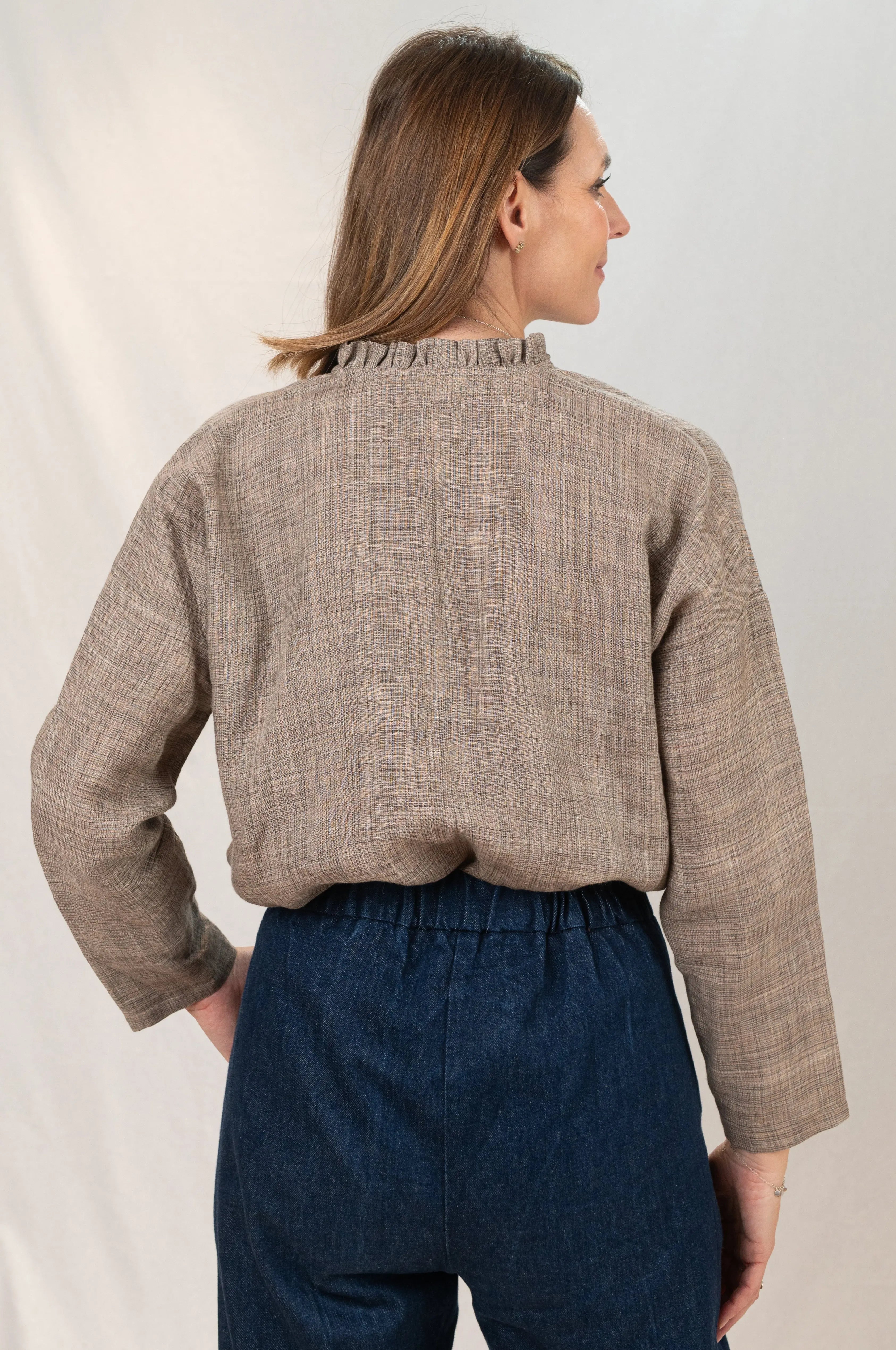Chemise Narcisse à col froncé en lin couleur grège naturel, vue de dos, portée avec un pantalon Sylène en denim bleu foncé, chemise portée blousée dans le pantalon.