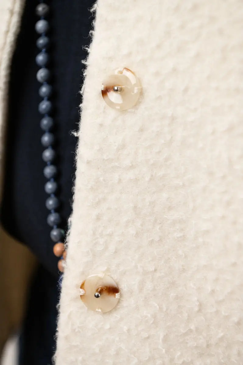 Gilet sans manches Ouessant réversible en drap de laine Casentino crème, détail des boutons effet corne, porté avec une chemise Narcisse en étamine de laine bleu marine et un collier Mala signé Nadine Tombez.