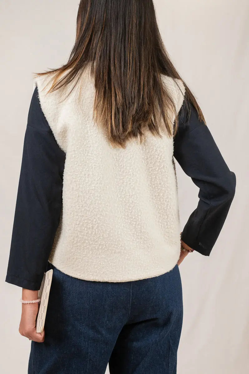 Gilet sans manches Ouessant réversible en drap de laine Casentino crème, vu de dos, porté avec une chemise Narcisse en étamine de laine bleu marine et un pantalon Sylène en denim bleu foncé.