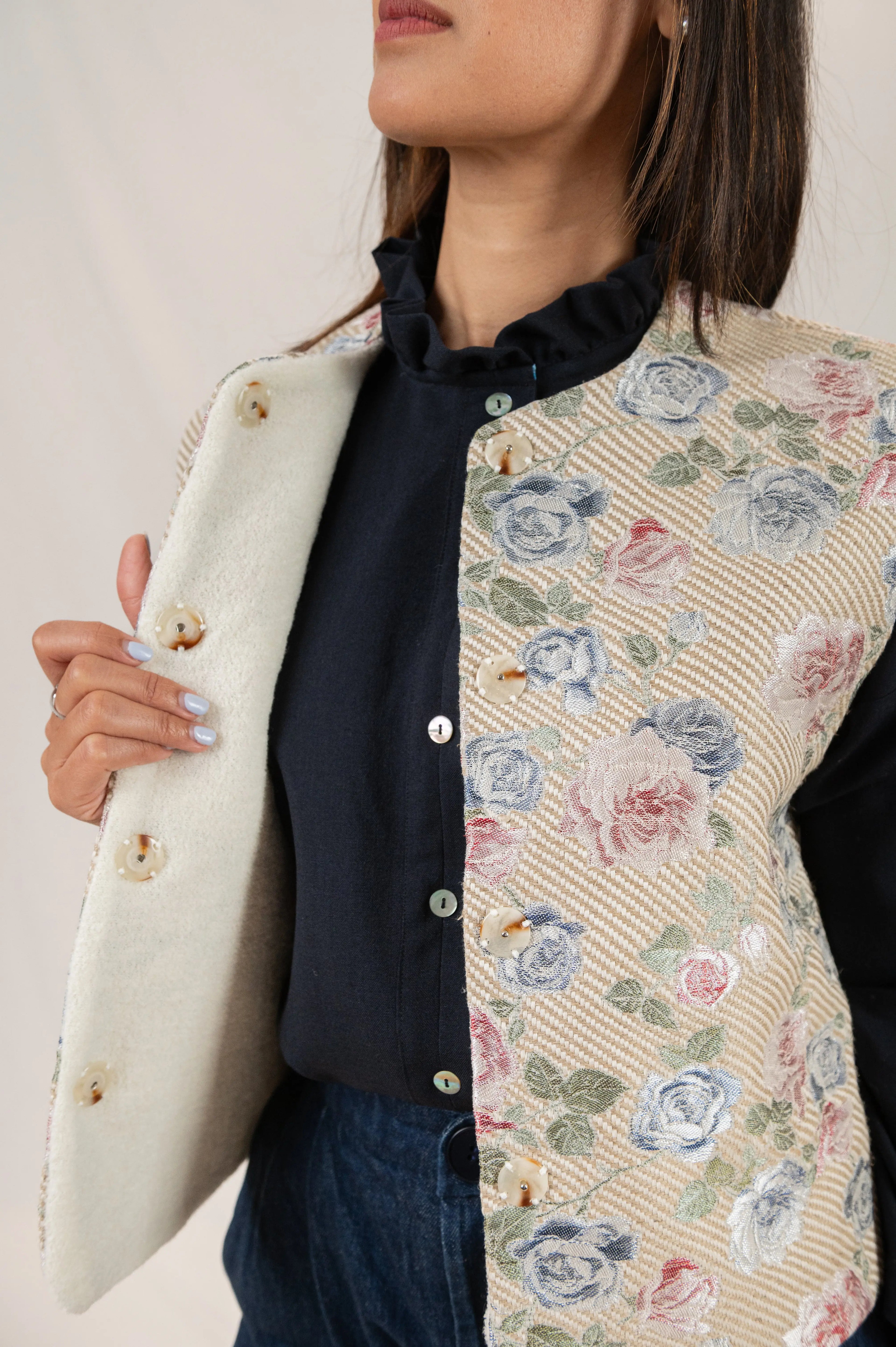 Gilet sans manches Ouessant en jacquard fleuri, détail de la coupe réversible, porté sur une chemise Narcisse bleu marine en étamine de laine et un pantalon Sylène en denim bleu foncé.