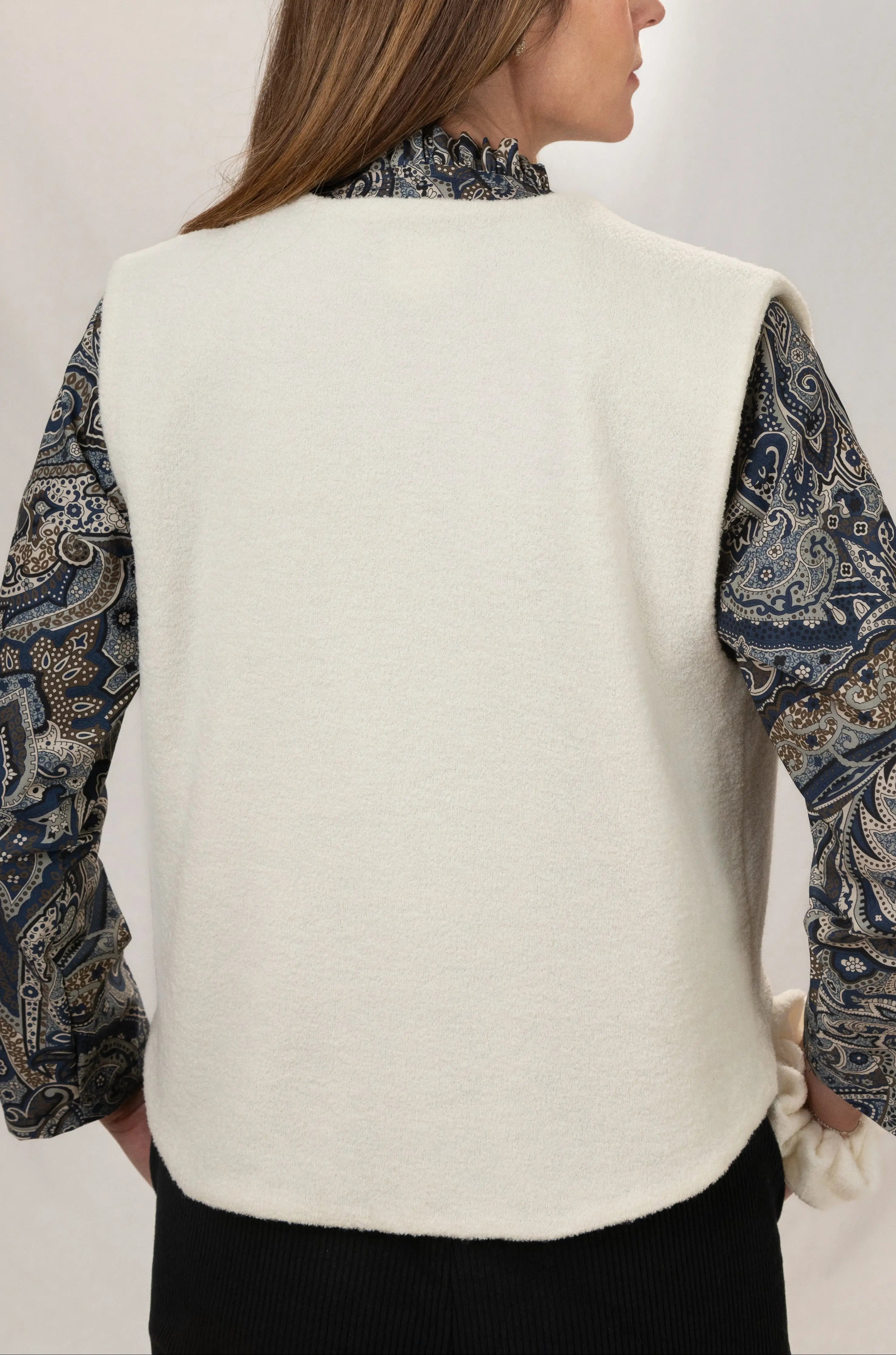 Gilet sans manches Ouessant en jersey de laine couleur crème, vu de dos, réversible, porté avec le pantalon Sylène en velours noir et une chemise Narcisse en popeline de coton à motif paisley cashmere.