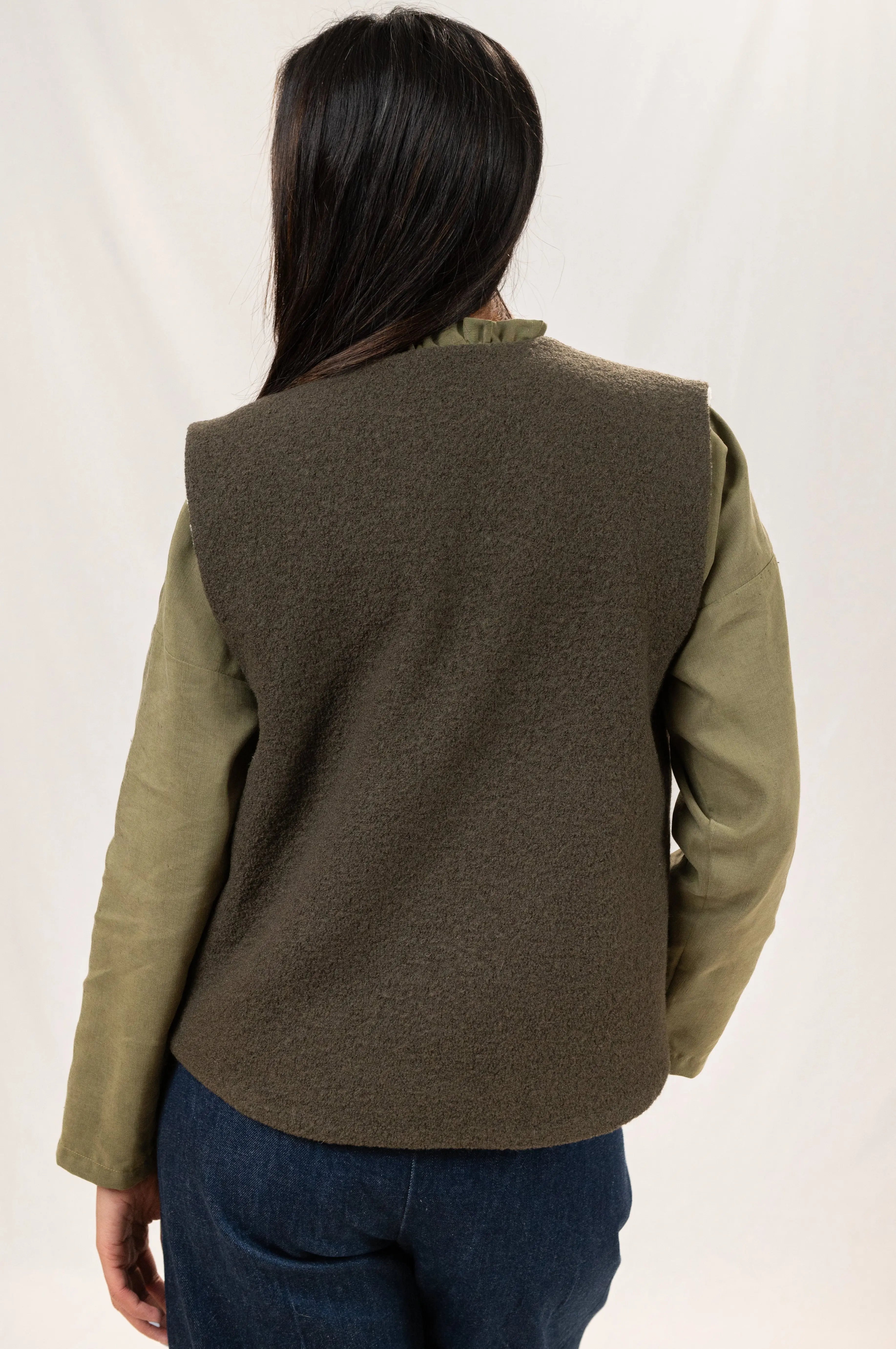 Gilet sans manches Ouessant réversible en laine bouillie vert forêt, vu de dos, détail de la coupe dos recouvrant, porté sur une chemise Narcisse en lin et soie kaki et un pantalon Sylène en denim taille haute, coupe Barrel Leg.