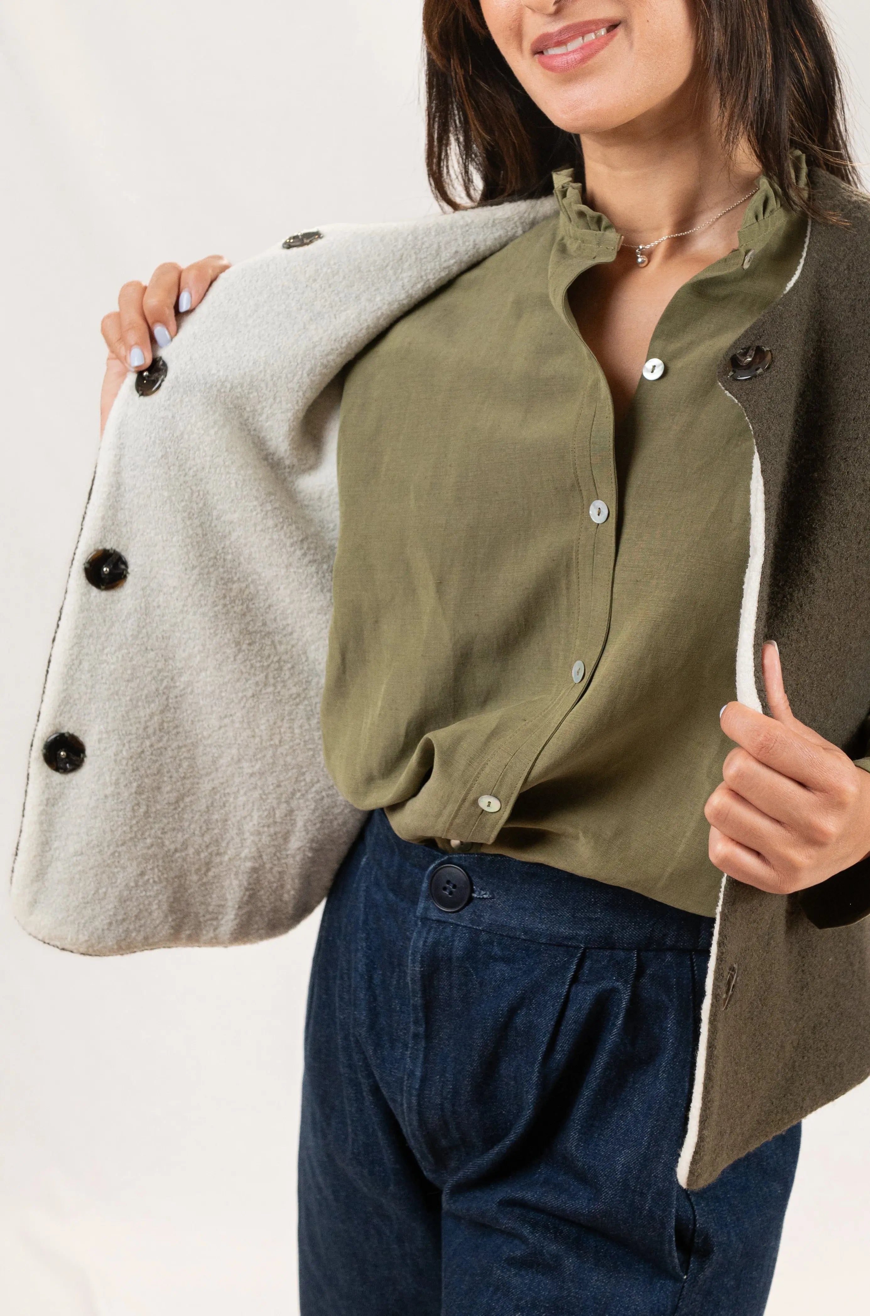 Gilet sans manches Ouessant en laine bouillie vert forêt, détail de la face réversible en jersey de laine couleur crème, porté avec une chemise Narcisse en lin et soie couleur kaki et un pantalon Sylène en denim taille haute.