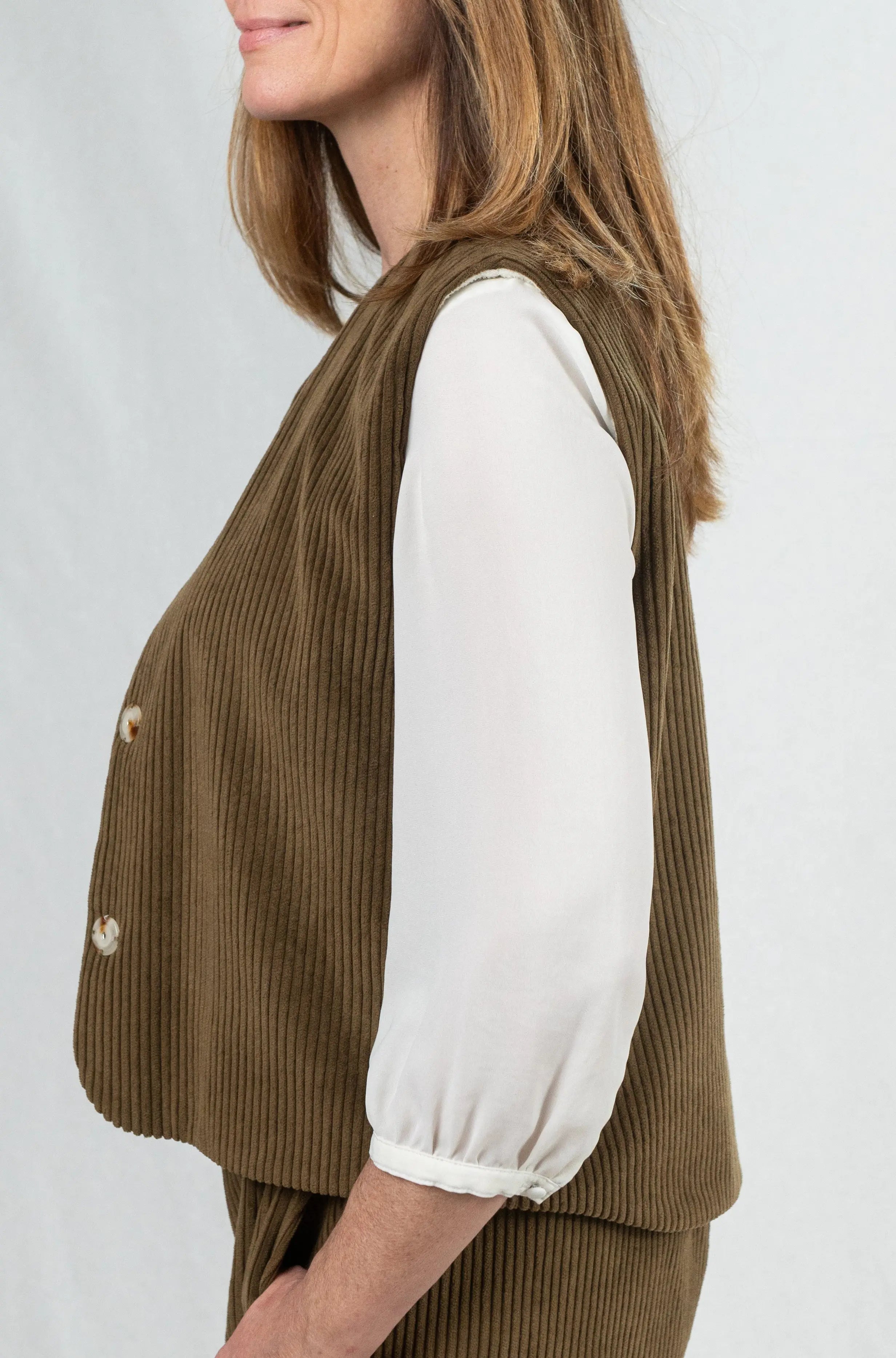 Gilet sans manches reversible Ouessant en velours marron havane, vu de profil, avec bouton effet corne, porté avec un pantalon assorti en velours côtelé marron havane, pour un total look inspiré du style tailleur.