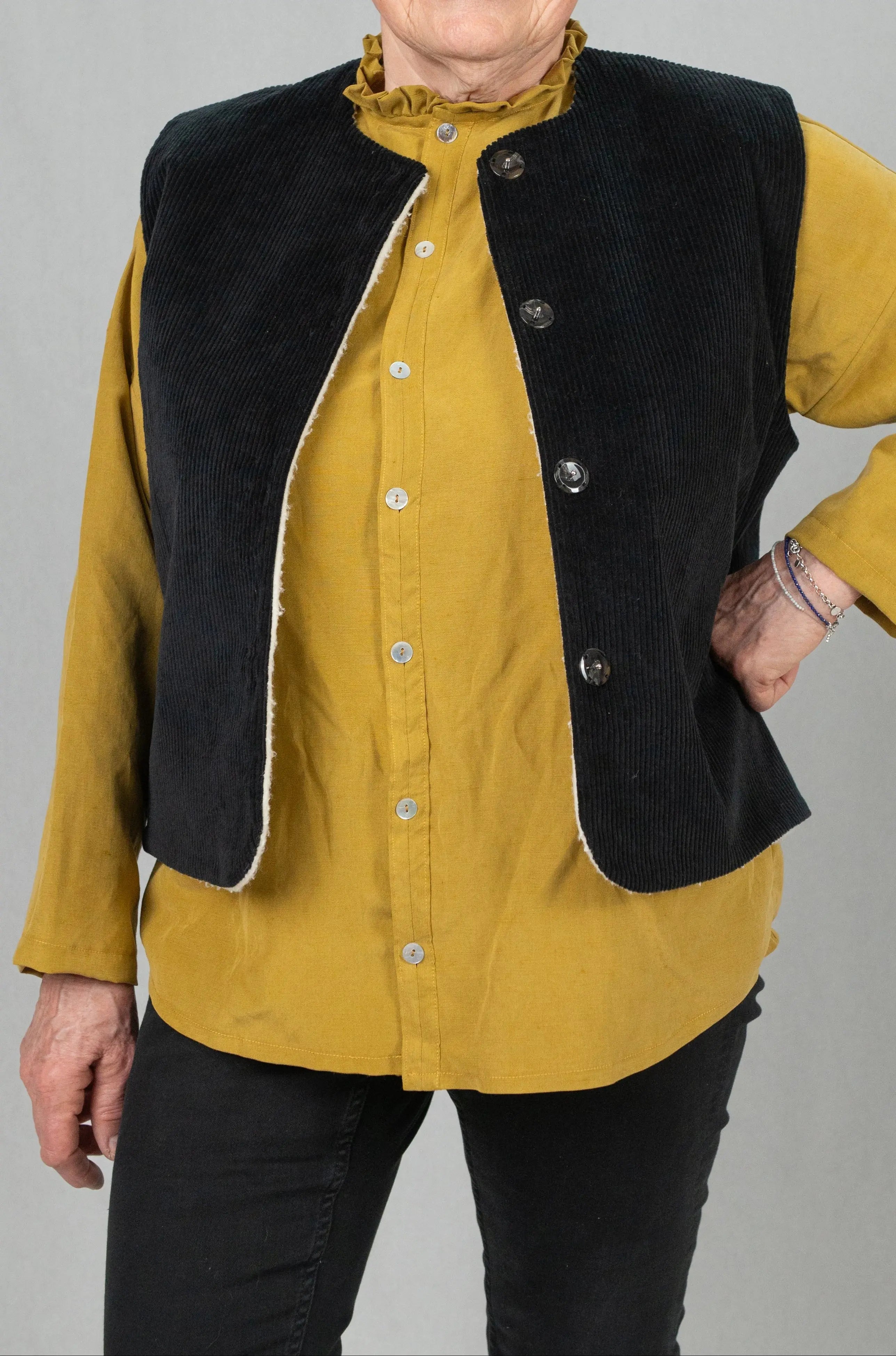 Gilet sans manches Ouessant réversible en velours noir, vu de face, porté avec une chemise Narcisse en lin et soie couleur moutarde et un pantalon slim noir.
