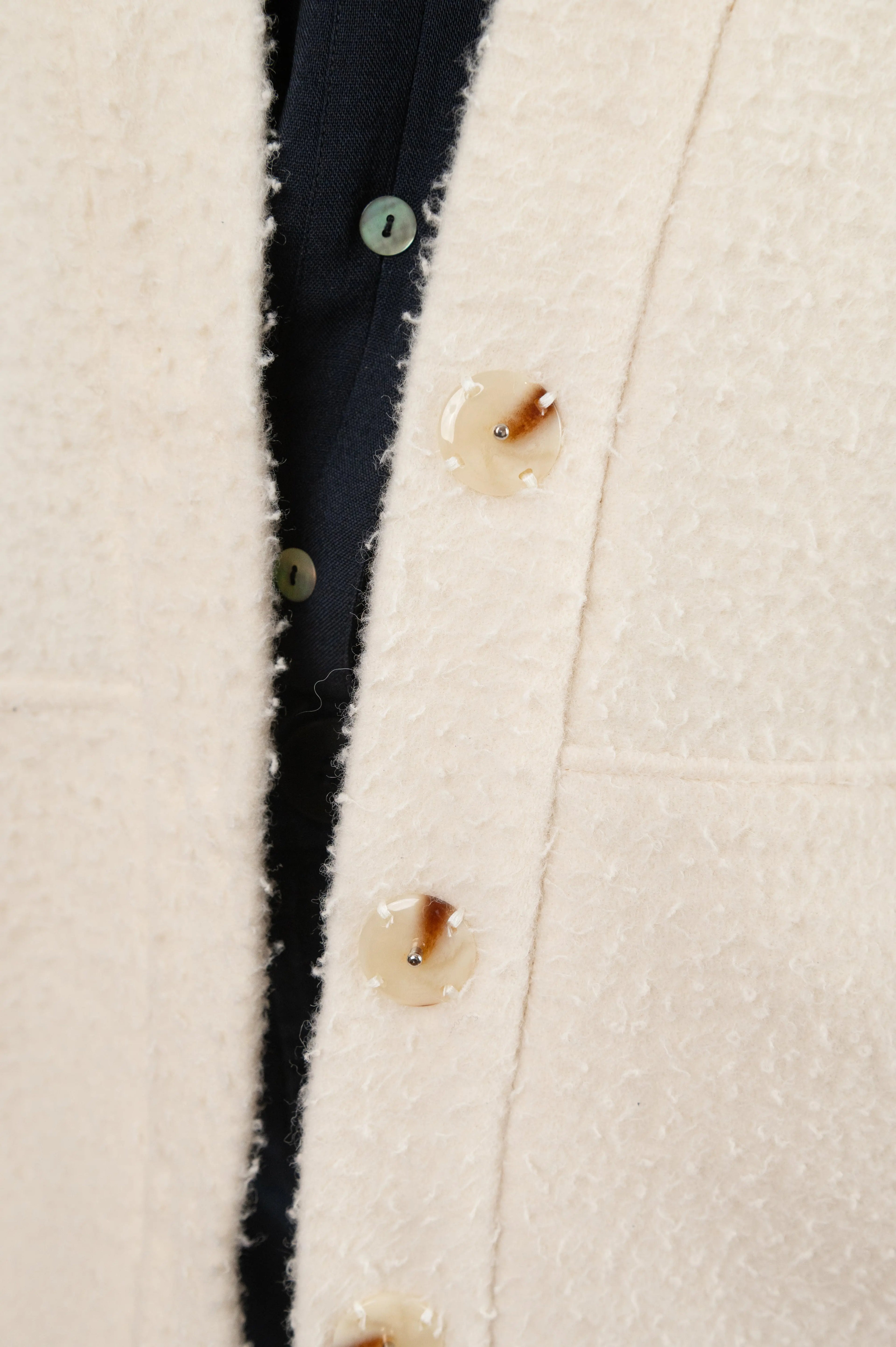 Manteau Cévennes coupe kimono en drap de laine Casentino crème, détail des boutons effet corne, porté avec une chemise Narcisse en étamine de laine bleu nuit.