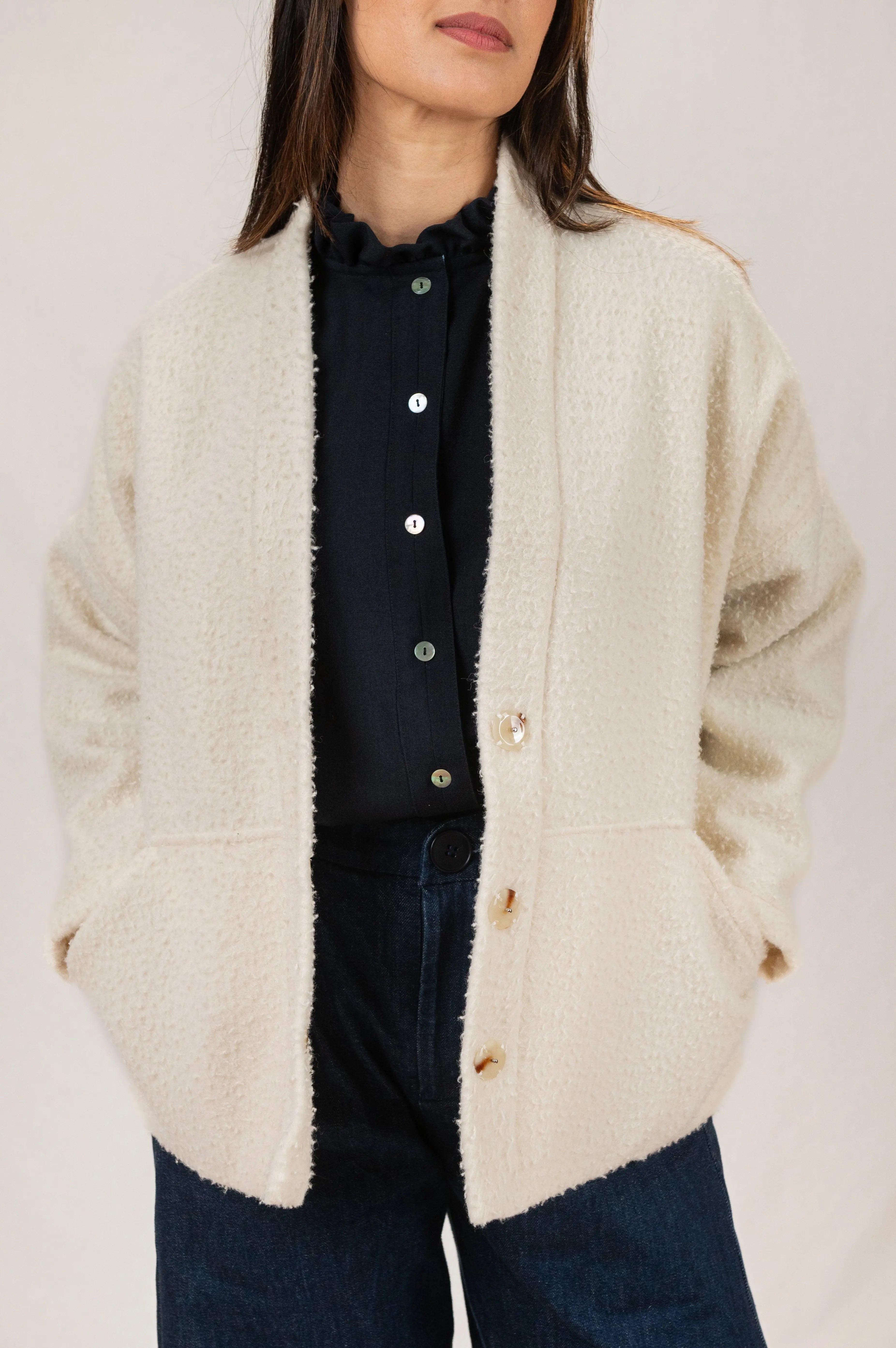Manteau Cévennes coupe kimono en drap de laine Casentino crème, vue de face, détail des boutons effet corne, porté avec une chemise Narcisse en étamine de laine bleu nuit et un pantalon Sylène en denim, coupe Barrel Leg.