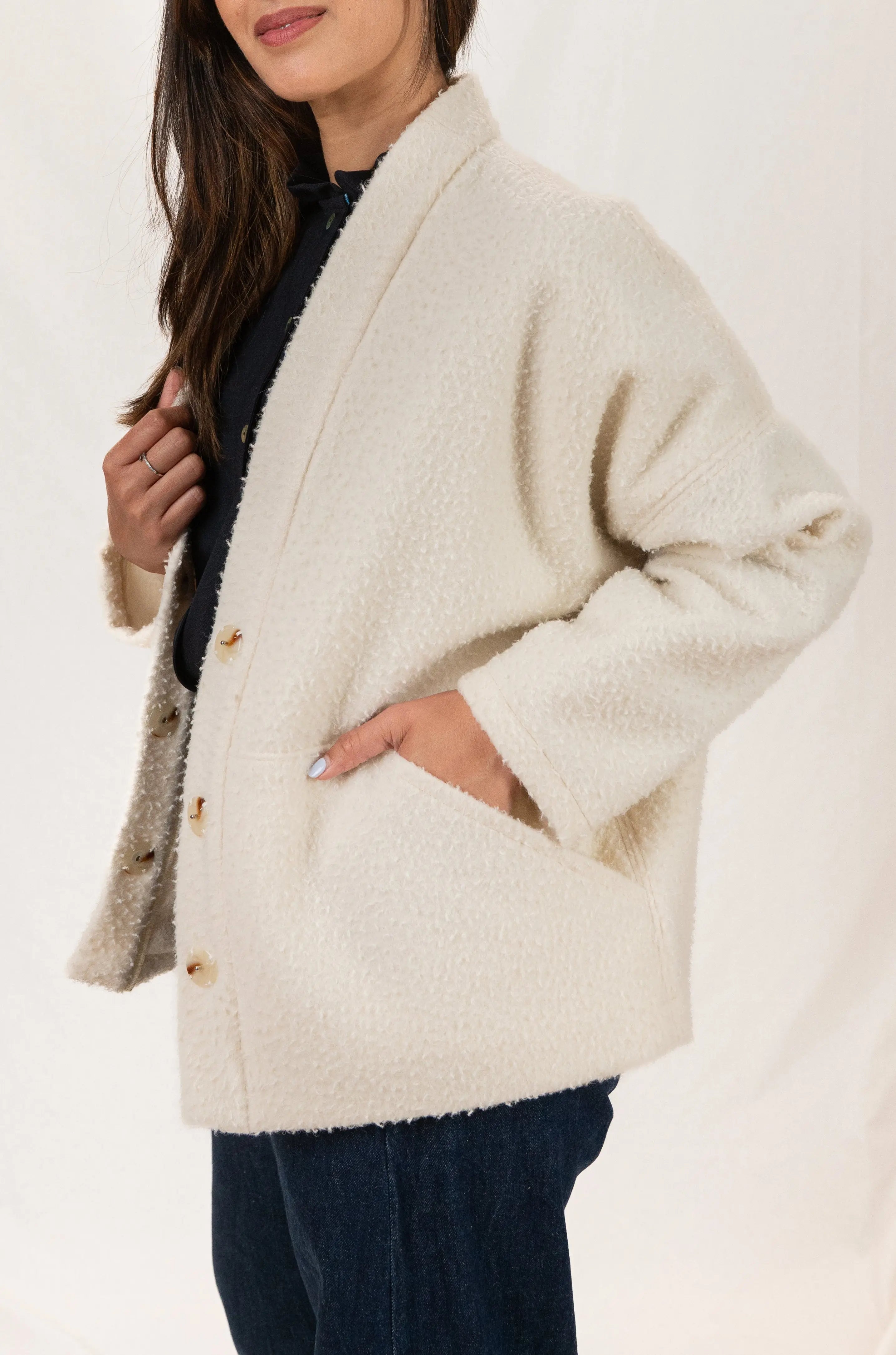 Manteau Cévennes coupe kimono en drap de laine Casentino crème, vue de profil, détail des boutons effet corne et de la découpe poche, porté avec une chemise Narcisse en étamine de laine bleu nuit et un pantalon Sylène en denim, coupe Barrel Leg.