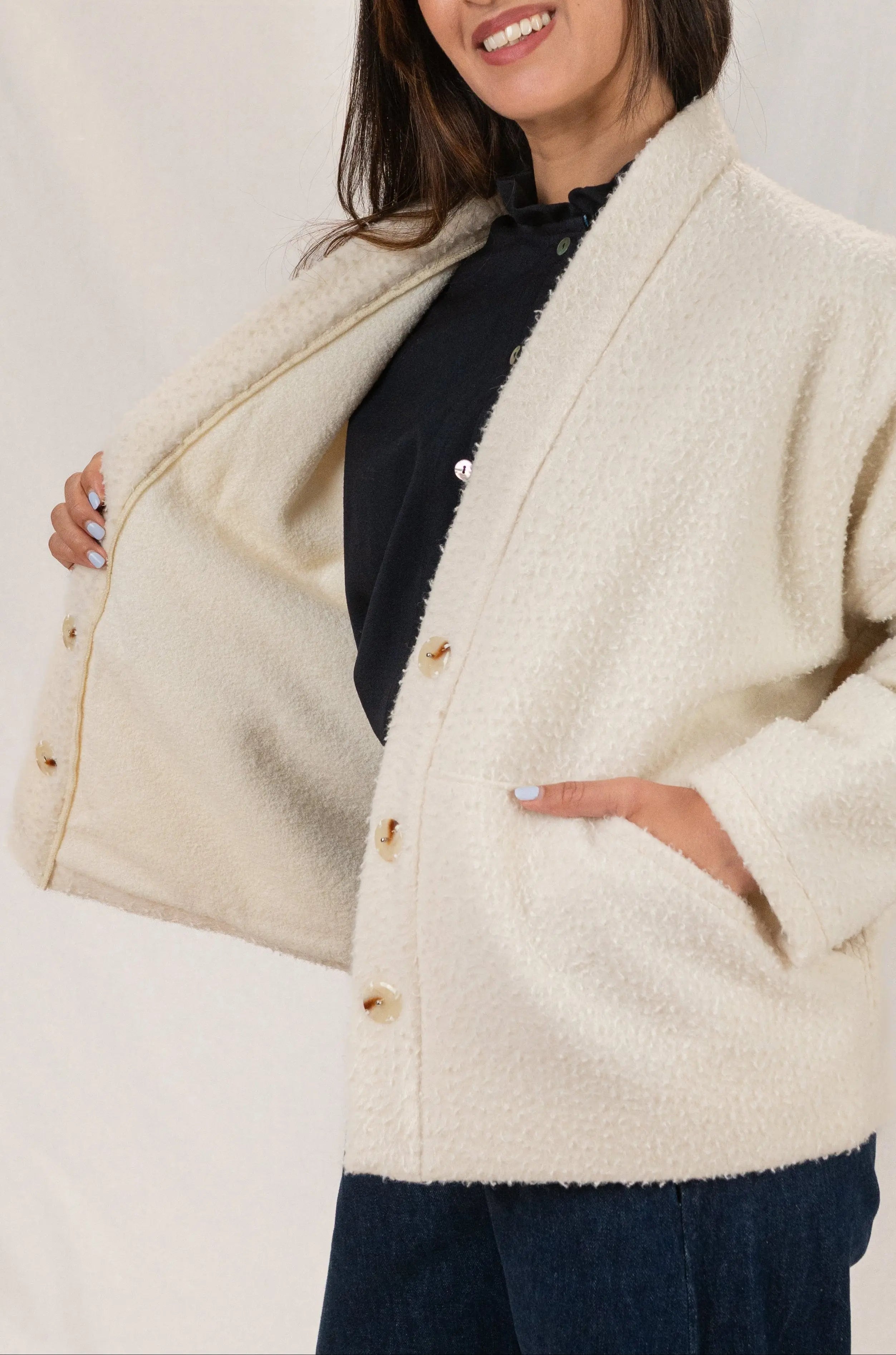 Manteau Cévennes coupe kimono en drap de laine Casentino crème, vu de profil, détail de la doublure en jersey de laine, porté avec une chemise Narcisse en étamine de laine bleu nuit et un pantalon Sylène en denim, coupe Barrel Leg.