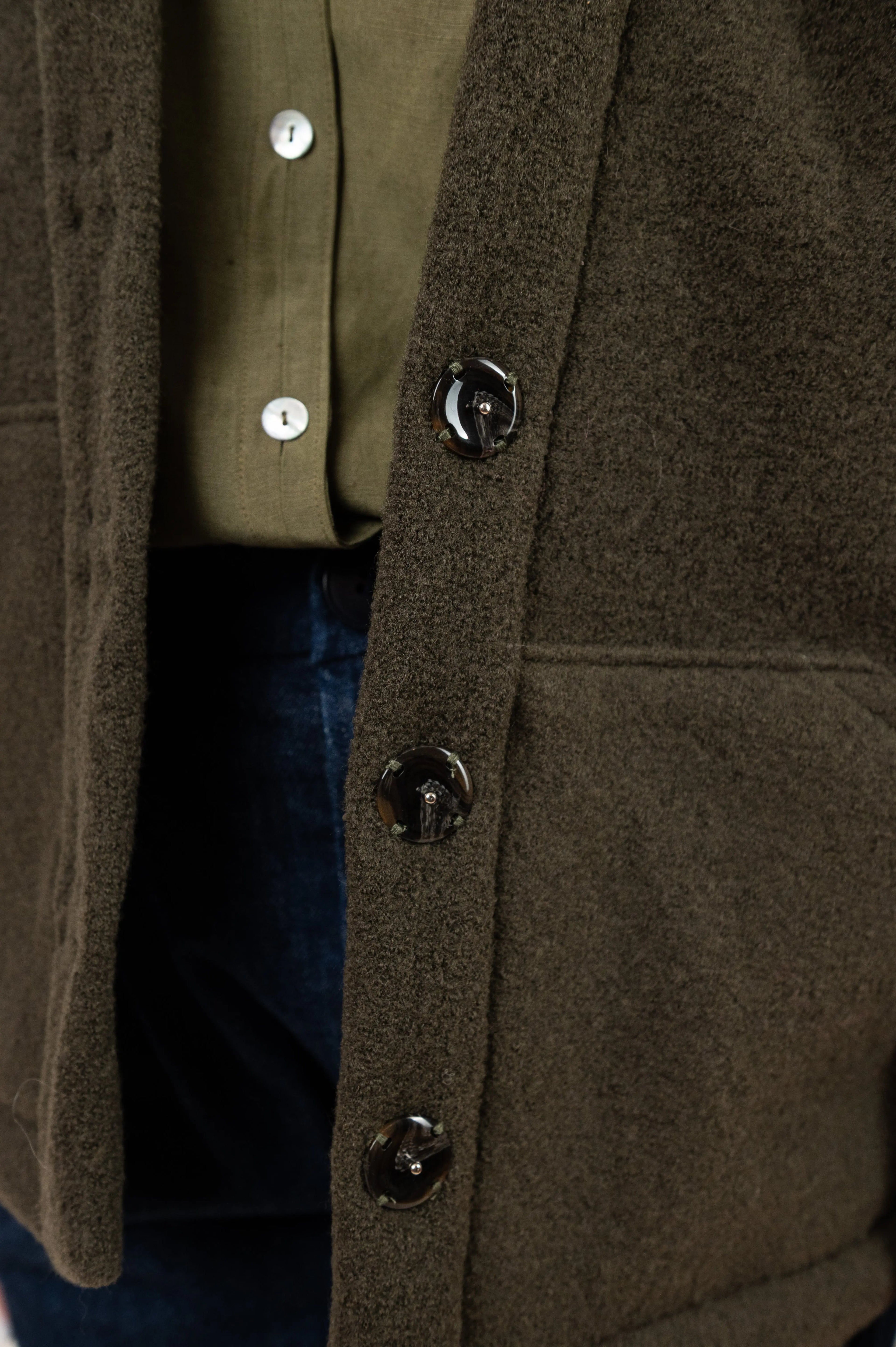 Manteau Cévennes coupe kimono en laine bouillie vert forêt, détail du bouton pression effet corne, porté avec une chemise Narcisse en lin et soie kaki et un pantalon Sylène en denim bleu foncé.