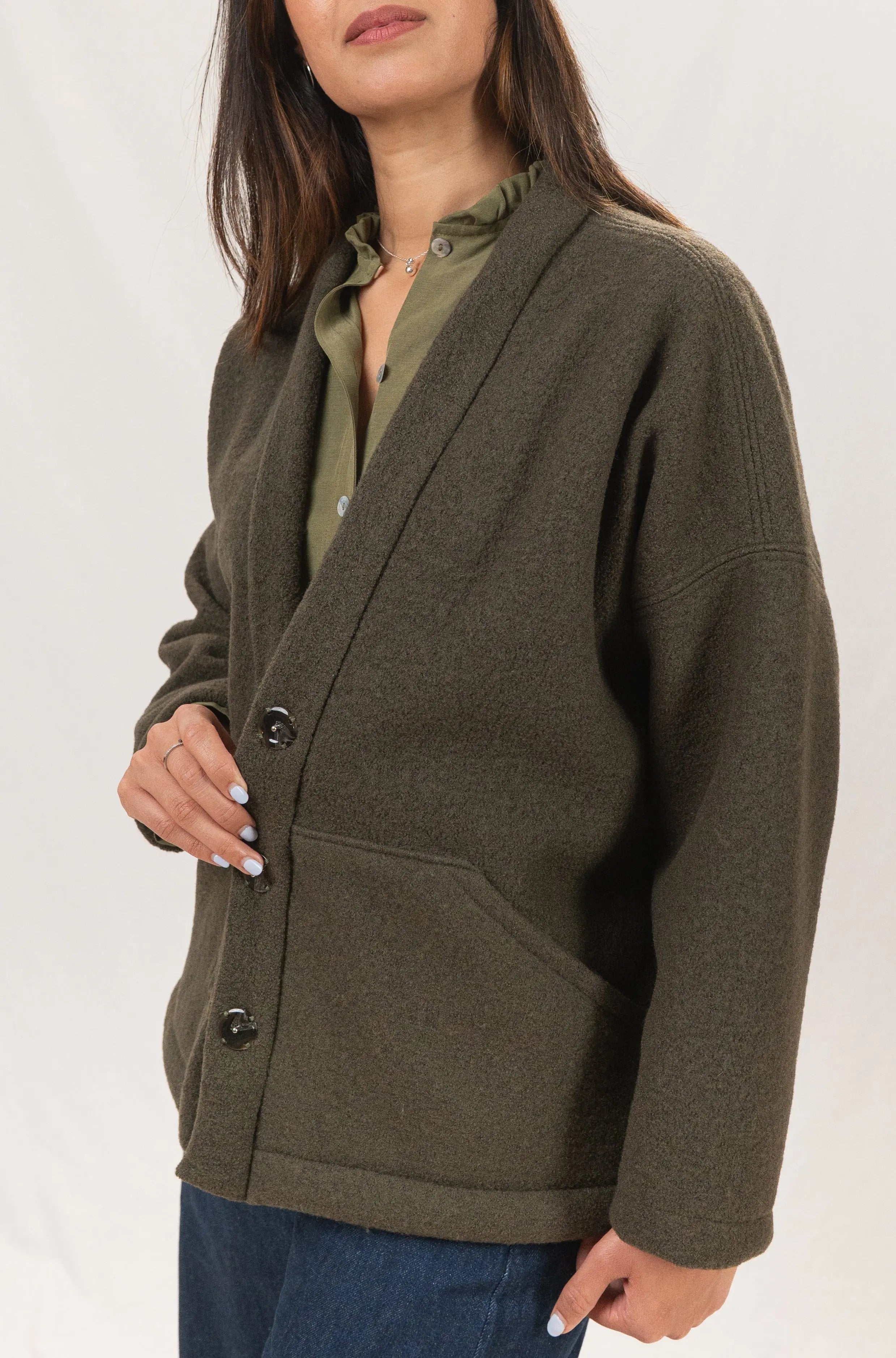 Manteau Cévennes coupe kimono en laine bouillie vert forêt, vue de profil, détail de la découpe de la poche, porté avec une chemise Narcisse en lin et soie kaki, un pantalon Sylène en denim bleu foncé, coupe Barrel Leg, et un collier signé A.no.