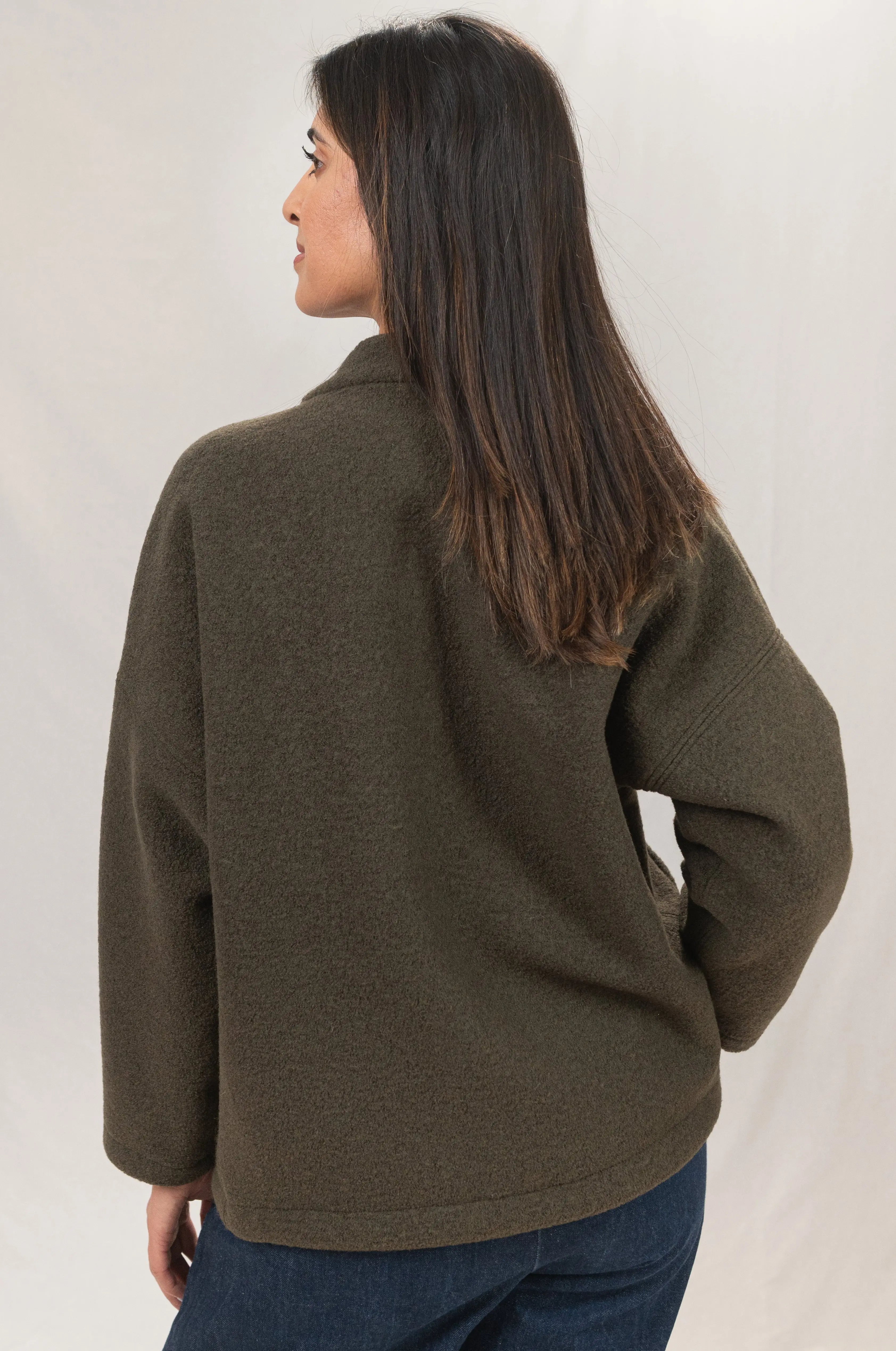 Manteau Cévennes coupe kimono en laine bouillie vert forêt, vu de dos, porté avec une chemise Narcisse en lin et soie kaki et un pantalon Sylène en denim bleu foncé, coupe Barrel Leg.