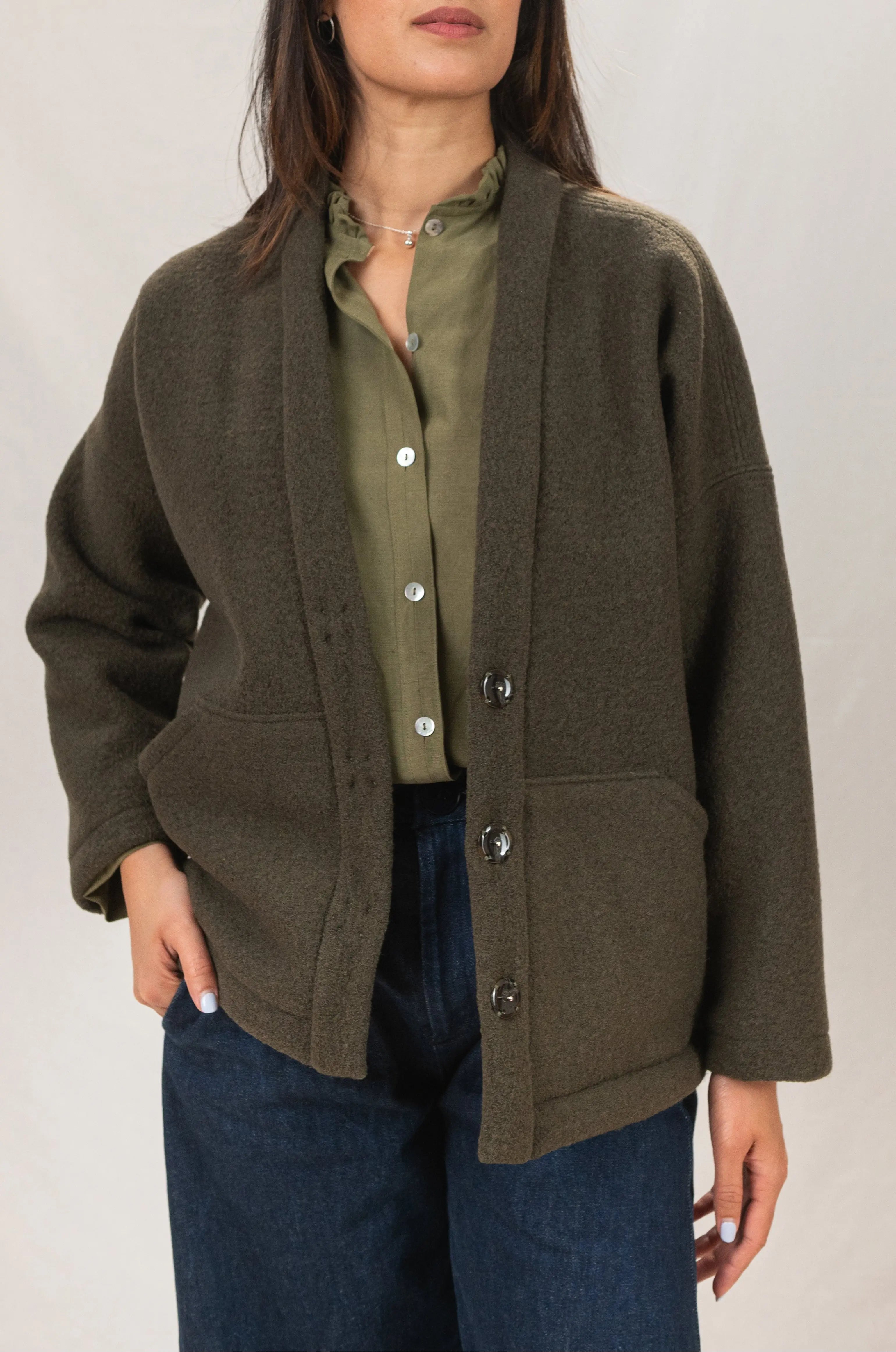 Manteau Cévennes coupe kimono en laine bouillie couleur vert forêt, vue de face, porté avec une chemise Narcisse en lin et soie kaki, un pantalon Sylène en denim coupe Barrel Leg bleu foncé et un collier signé A.no.