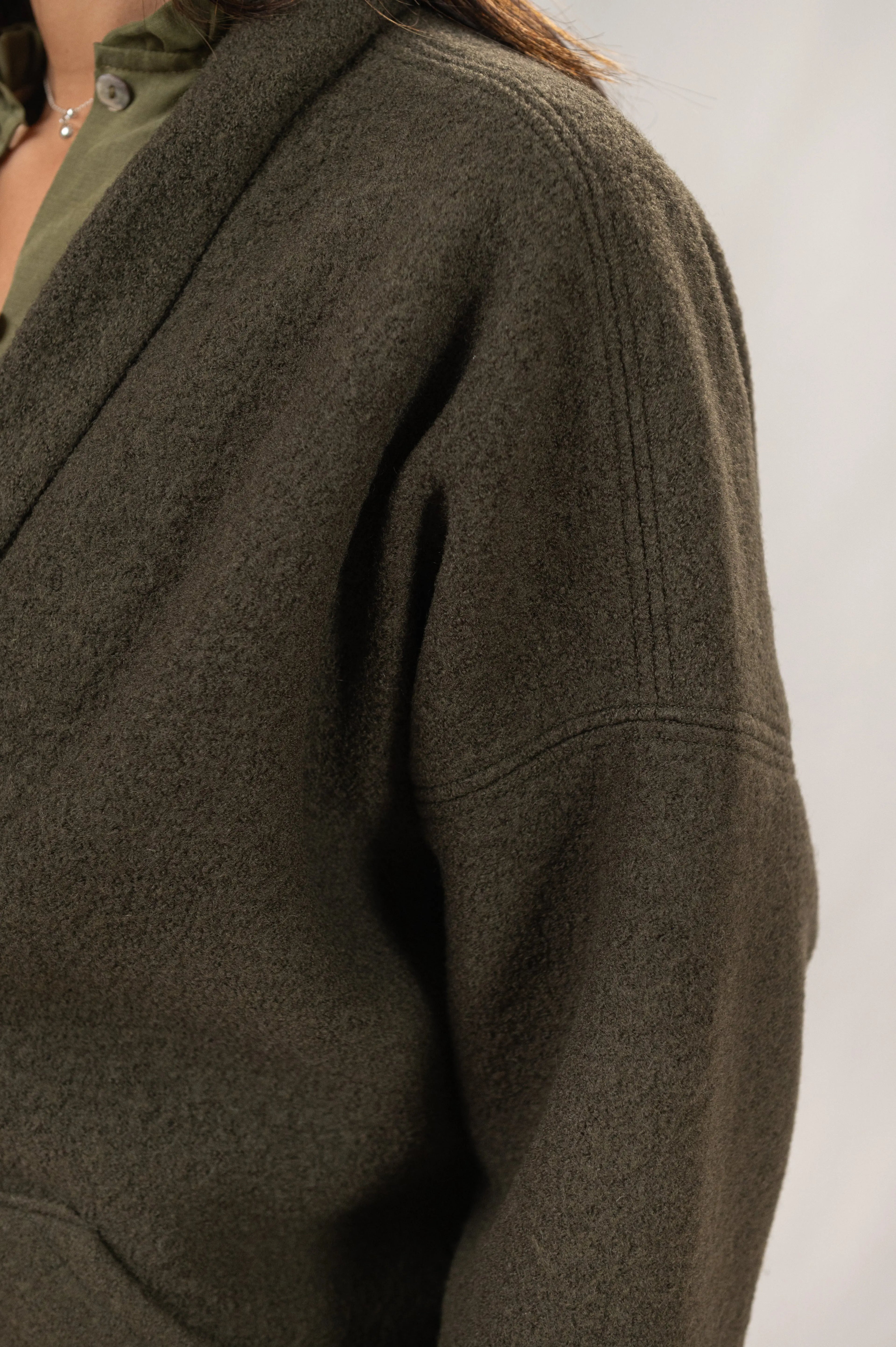 Manteau Cévennes coupe kimono en laine bouillie vert forêt, détail de la tête d’épaule, porté avec une chemise Narcisse en lin et soie kaki et un collier signé A.no.