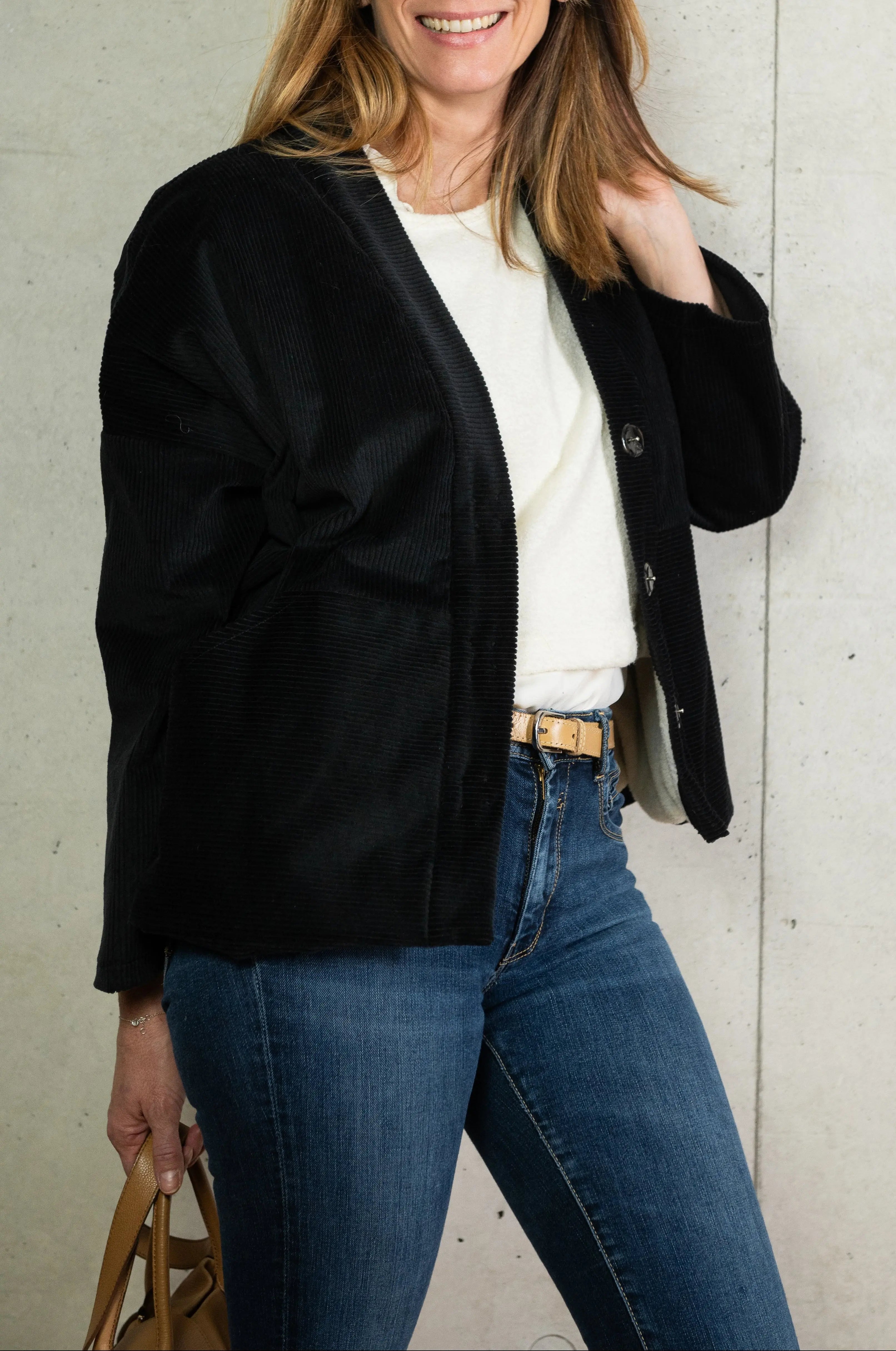 Manteau Cévennes coupe kimono en velours côtelé noir, vu de profil, porté avec un pull Mousse en jersey de laine crème et un bracelet signé A.no.