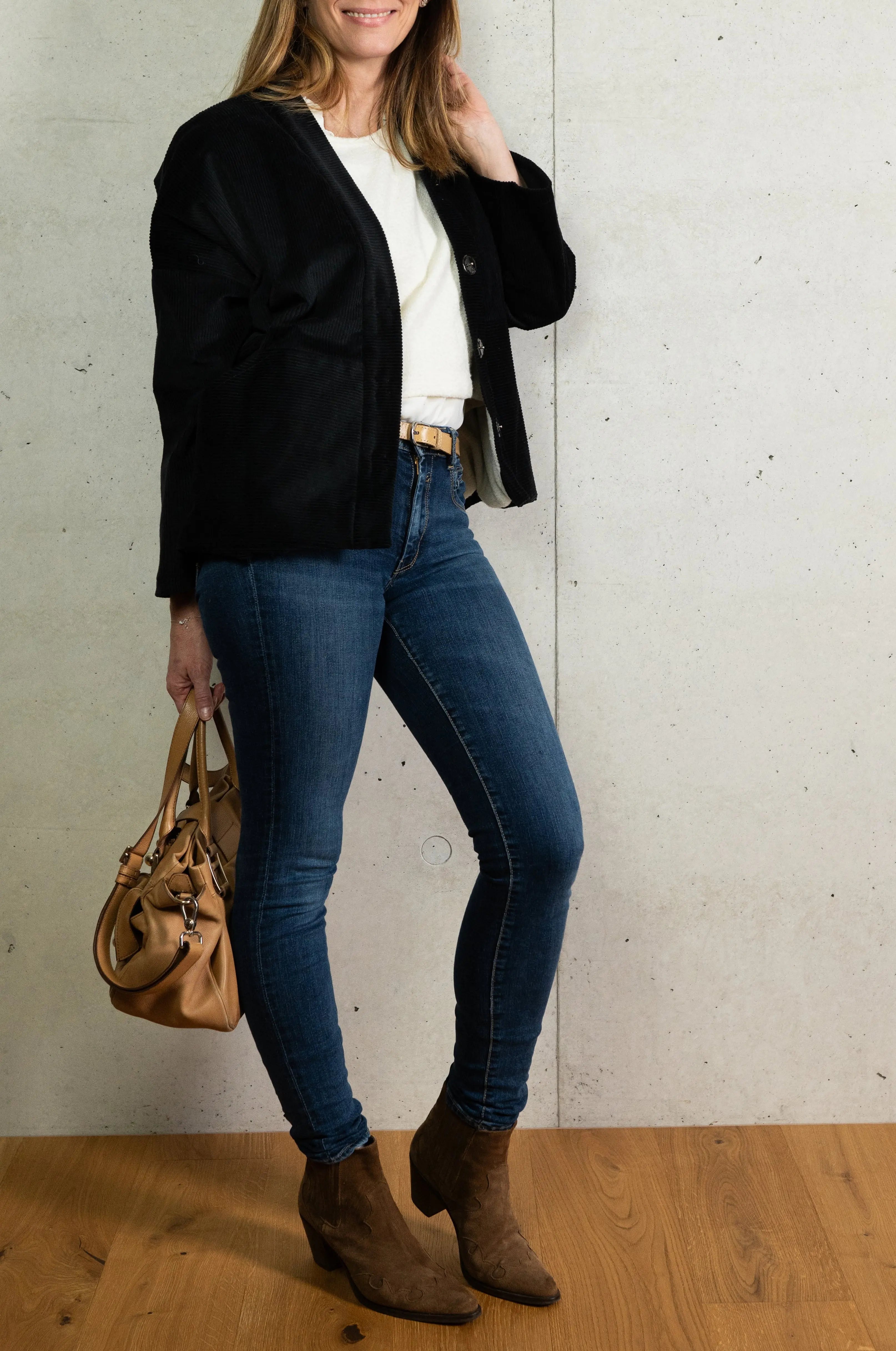 Manteau Cévennes coupe kimono en velours côtelé noir, vu de profil avec aperçu de la doublure crème en Jersey de laine porté avec un pull Mousse en jersey de laine crème et un bracelet signé A.no.