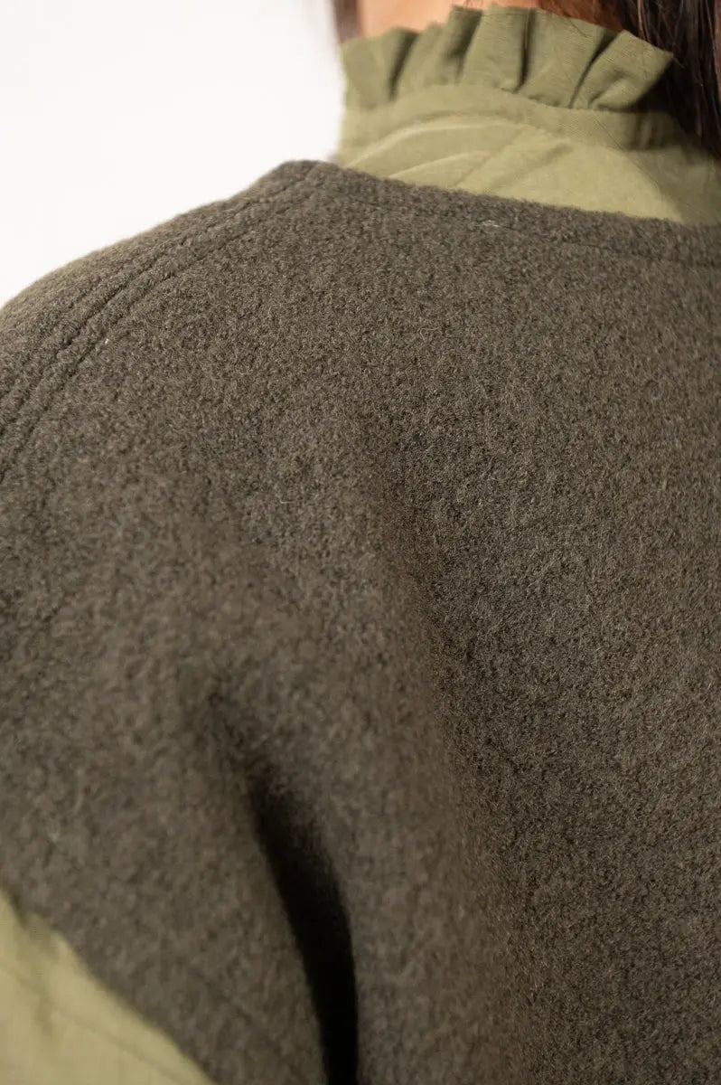Pull Mousse manches courtes vert forêt en laine bouillie, avec détail de la surpiqûre et aperçu du col froncé de la chemise Narcisse kaki.